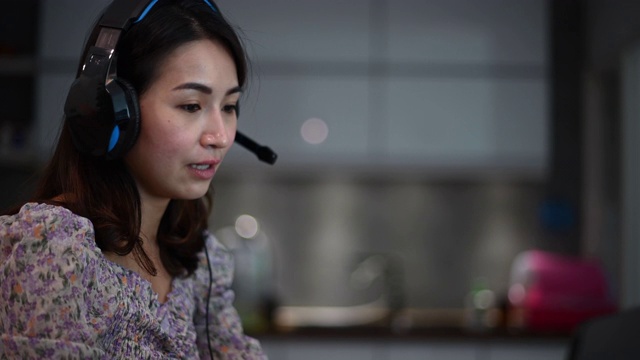 一位亚洲的中国美女在家工作，作为客户服务，用笔记本电脑和耳机在厨房打字，在线回答她的客户视频素材