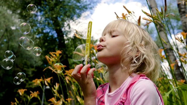 一个快乐的金发小孩在夏天的公园里吹肥皂泡。缓慢的运动。高清视频素材