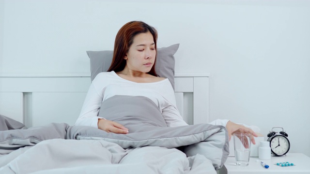 一名年轻的亚洲女子在家中卧病在家吃药的4K视频视频素材