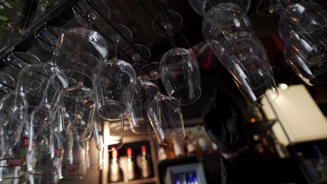 一个年轻的酒保拿起挂着的酒杯的慢镜头视频素材