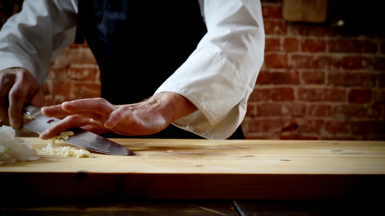 厨师在菜板上切两瓣大蒜准备食物。4 k视频下载