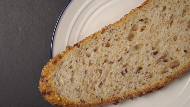 一片新鲜的谷物面包放在带蓝色边框的白色盘子里。视频下载