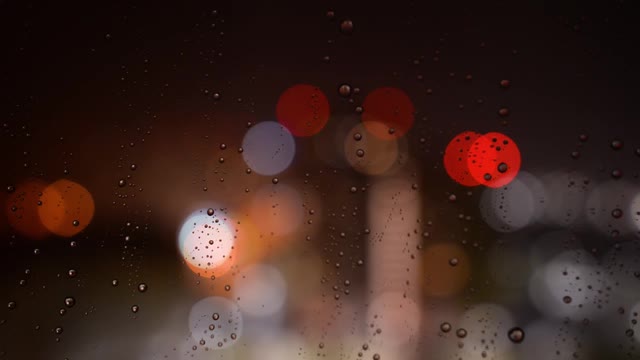 夜里雨点从玻璃上滚下来。雨点落在散景背景的玻璃上。窗外夜雨绵绵视频素材