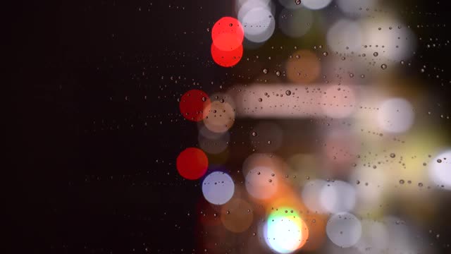 夜里雨点从玻璃上滚下来。雨点落在散景背景的玻璃上。窗外夜雨绵绵视频素材