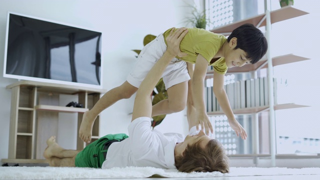 无忧无虑爱的家庭大人爸爸抱着可爱的小孩儿子假装超级英雄飞机躺在地板上玩视频素材