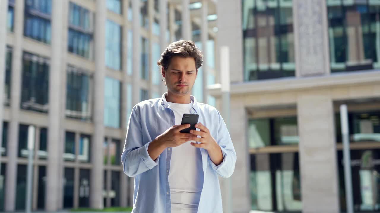 放大中景的白人青年站在街上，短信手机和微笑视频下载