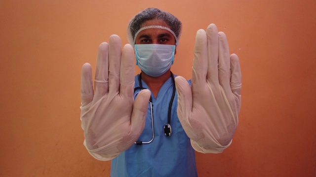 医生在橙色的背景下做着蓝色的手势，直视着摄像机视频下载