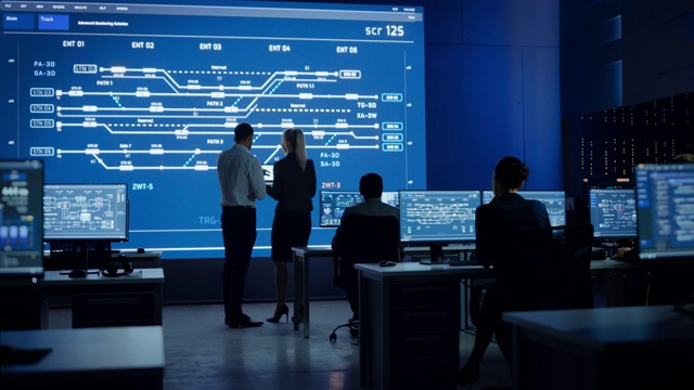 电信公司系统控制和监控室，由多元文化的专业人员组成的计算机团队。大屏幕显示显示基础设施信息图。后视图视频素材