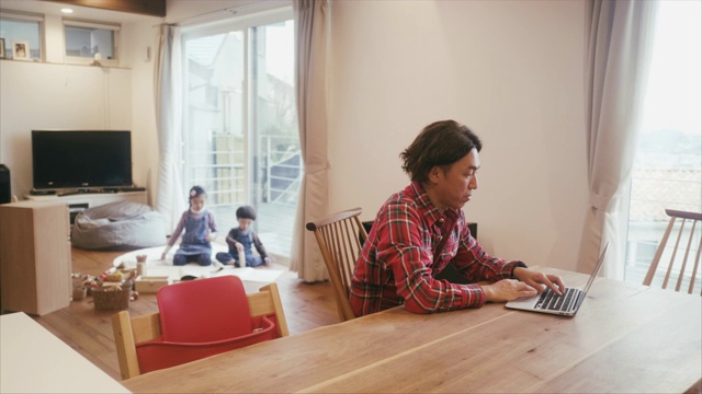 日本男人在家里工作，而孩子们在客厅玩视频下载