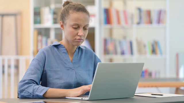 疲惫的非洲女人与笔记本电脑在图书馆背痛视频素材