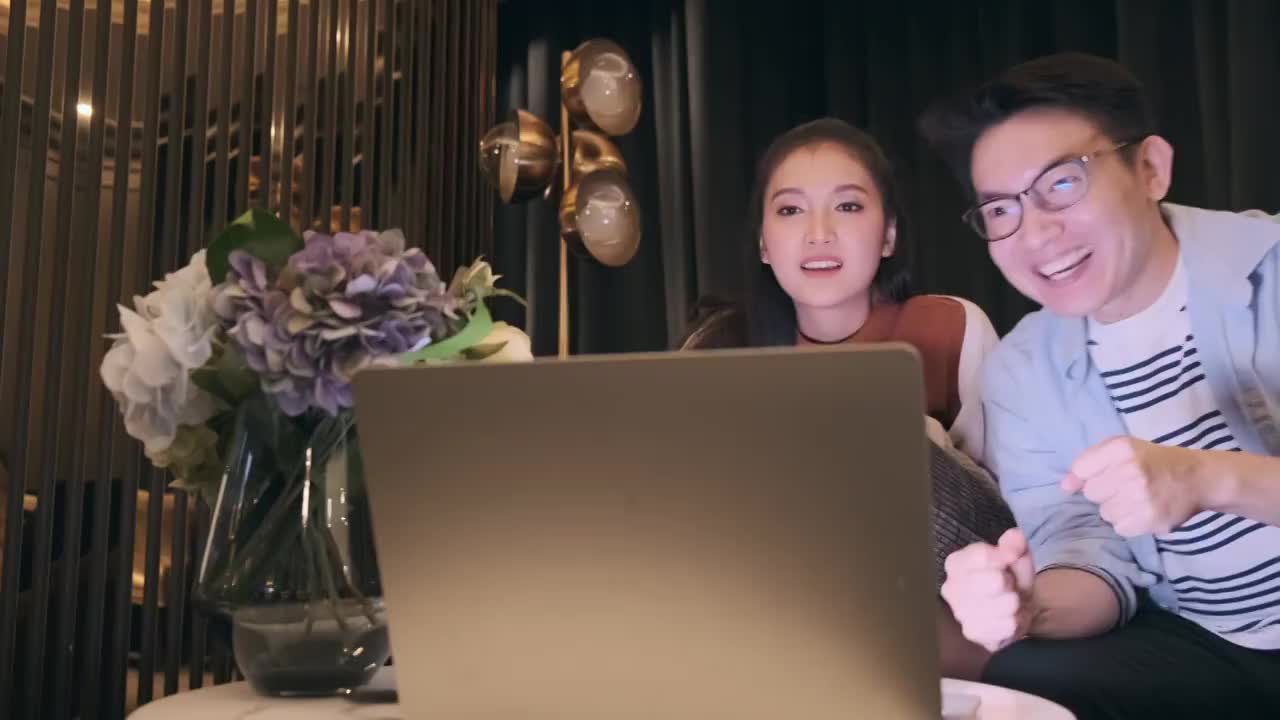 两个幸福的年轻亚洲夫妇结婚家庭享受周末休闲时刻休闲服装微笑笑啦啦队退出一起看电视游戏体育节目在客厅沙发上视频素材