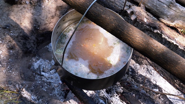 在一个旅游锅的火上烹饪。在篝火上挂的旅游圆顶礼帽视频素材
