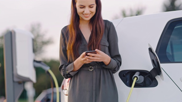 SLO MO快乐的女人在等待她的汽车充电时使用她的智能手机视频素材