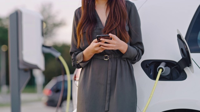 一个在给车充电时使用智能手机的女人视频素材