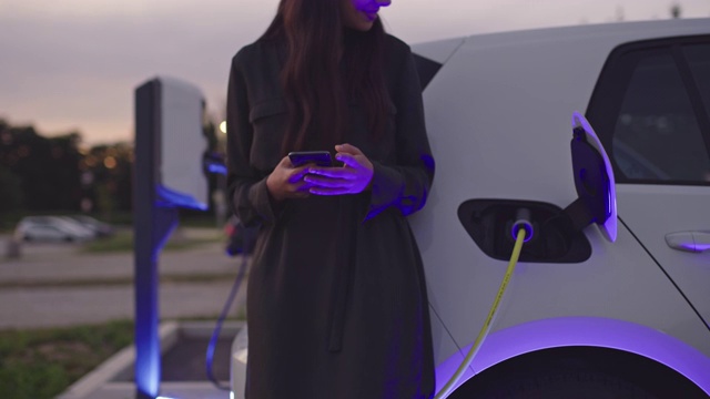SLO MO快乐的女人在等待她的汽车充电时使用她的智能手机视频素材
