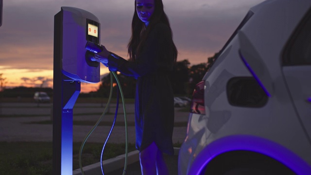 一名女子在充电站用蓝色能量将电动汽车插头插入她的汽车视频素材