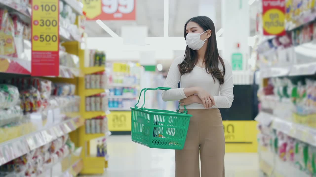 戴着口罩的女人在超市购物和检查食品货架视频下载