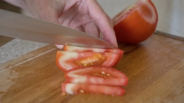 特写女人手握刀切，切红番茄。木切板上的切刀。素食主义者的饮食。春番茄碎。在厨房烹饪蔬菜。缓慢的运动。视频素材