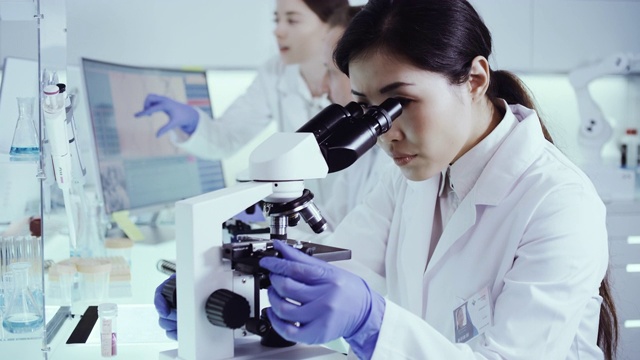 实验室小组处理病原体样本。亚洲女医生使用显微镜视频下载
