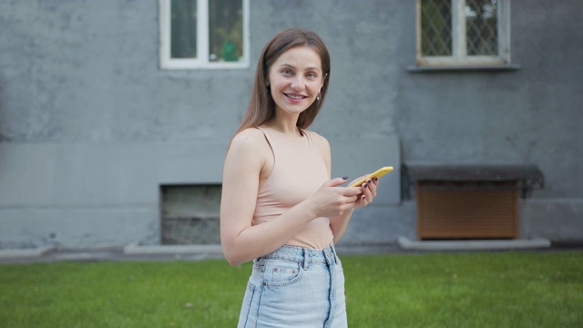 漂亮微笑的年轻女子在城市街道上使用她的手机。夏天的心情视频下载