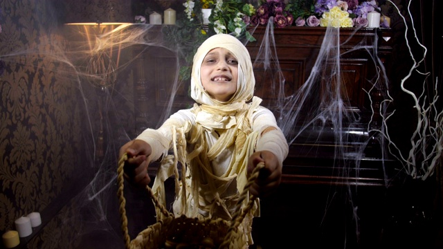 女孩穿着万圣节木乃伊服装和一个篮子在古老的黑暗哥特式室内跳舞，室内覆盖着蜘蛛网和神秘的雾，要求在那里提供一种享受。4K慢镜头50帧/秒视频下载