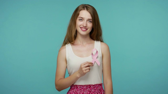 可爱善良的女孩穿着夏装，露出粉红色的丝带，对着镜头微笑，警告乳腺癌的风险视频下载