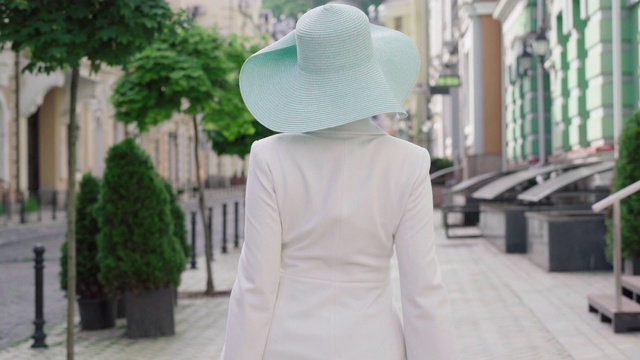 镜头跟随自信的时尚女士走在阳光明媚的城市街道上，转向镜头微笑。优雅时尚的白人妇女漫步在欧洲城市购物袋。视频下载