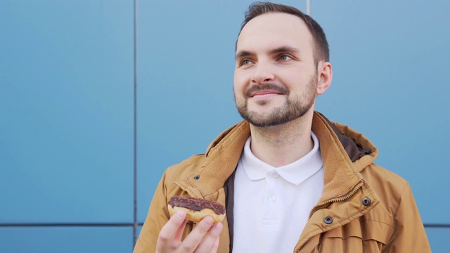 可爱的大胡子男子闻着巧克力甜甜圈，欣赏着它的香味视频下载
