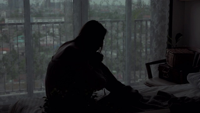 沮丧的年轻美丽的亚洲女人独自坐在公寓卧室的床上哭泣。孤独悲伤的女孩，想起悲伤烦恼。消极情绪与心理健康的概念。视频素材
