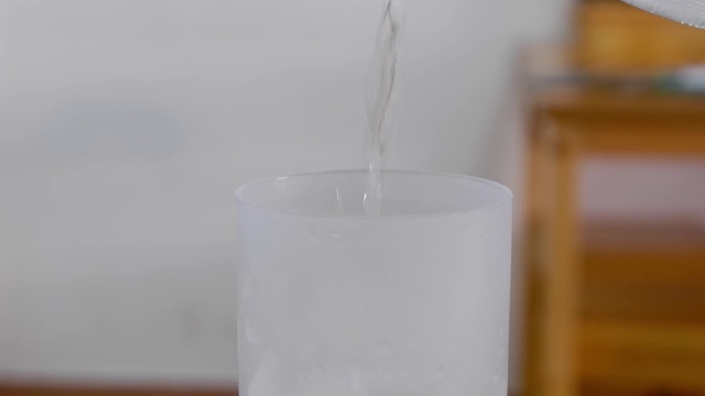 把水倒进木桌上一个加冰的玻璃杯里。视频下载