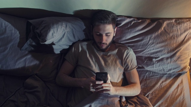 不眠之夜，无聊的男人在床上看书喂手机视频下载