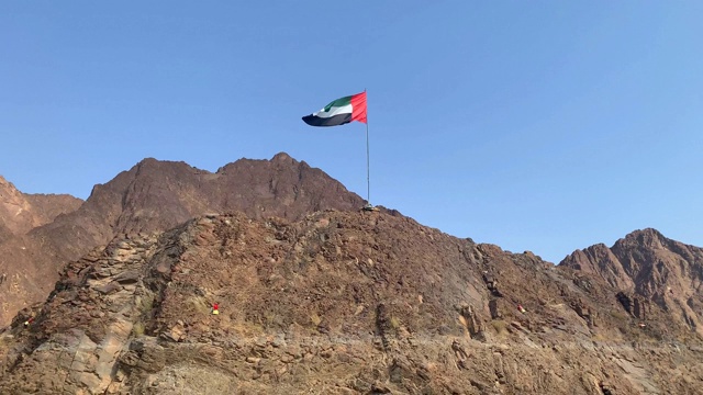 在蓝天的背景下，阿拉伯联合酋长国的国旗在哈塔湖中央的山顶飘扬。视频素材