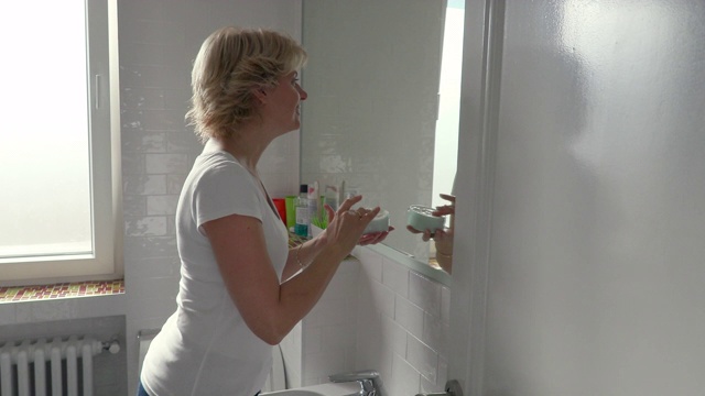 微笑的女人拿着罐子，在浴室里涂面霜视频素材
