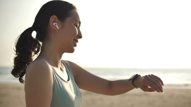 运动女性使用智能手表在海滩上晨练视频下载