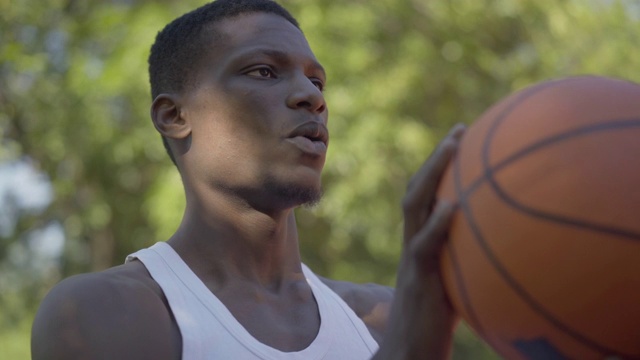 特写集中的非洲裔美国运动员把球扔进篮球圈。这是一个坚定的年轻人在夏天的户外球场上进行运动训练的肖像。视频素材