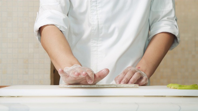 男厨师手在手套展开竹垫子在厨房做寿司的特写。视频素材