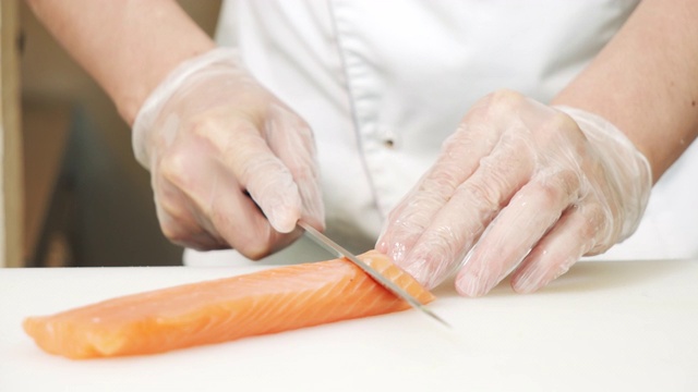 特写男厨师双手戴着手套，在白板上用刀切三文鱼片。视频素材