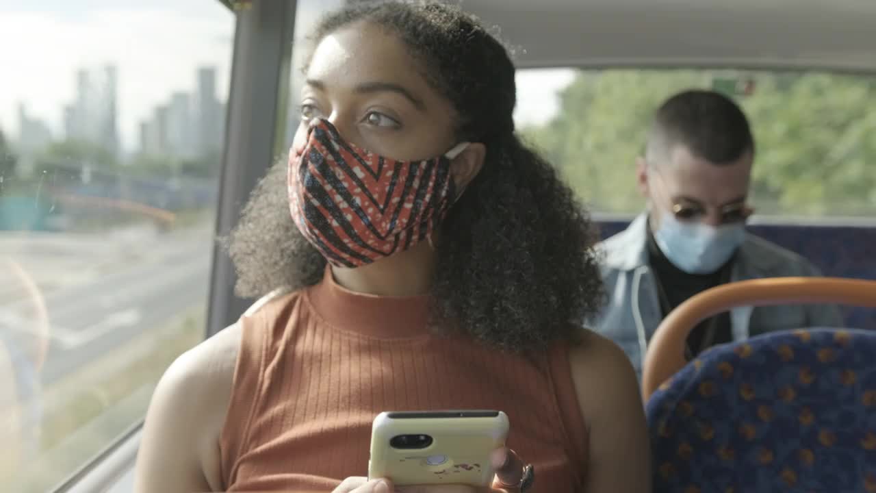 在冠状病毒大流行期间，年轻的非洲裔美国女性戴着口罩坐在公交车上视频素材