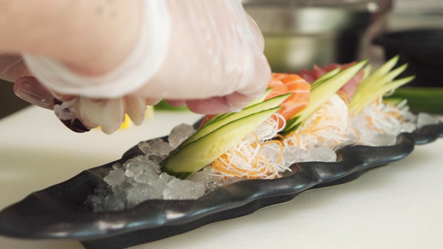 一个戴着手套的男性厨师的手在冰的基底上摆放着鱼、章鱼和蔬菜。视频素材