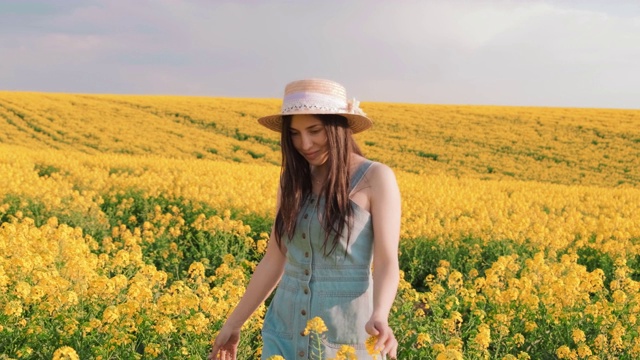 快乐的年轻漂亮的女子走在黄田油菜籽上，摸着鲜花的手视频下载