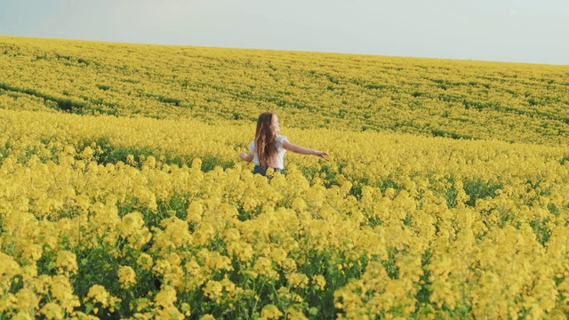 乡村的美丽迷人的女孩走在黄色的盛开的田野。少年笑着说视频素材