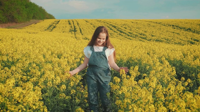 快乐的年轻快乐的可爱微笑的女孩走过春天盛开的黄色油菜地视频素材
