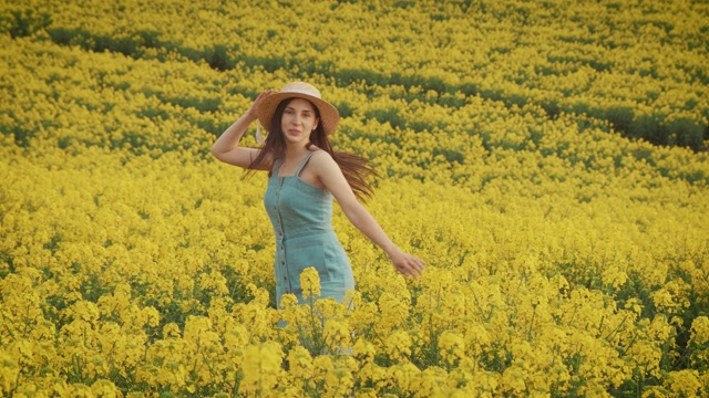 快乐年轻美丽的女子走在黄花田里，油菜籽开花了视频素材