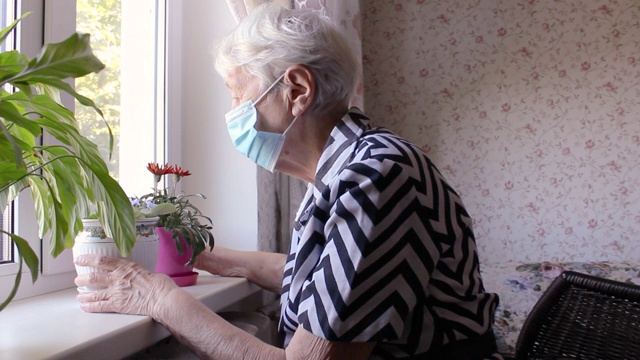 2019冠状病毒病、健康、安全和大流行概念——坐在窗边的孤独老年妇女视频下载