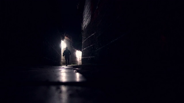 夜晚，一个人的剪影沿着漆黑的小巷人行道奔跑视频素材