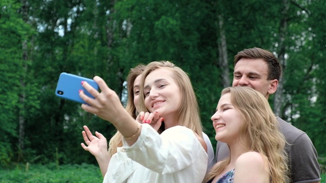 人们在空地上用智能手机自拍，在野餐时摆姿势拍照大笑。视频素材