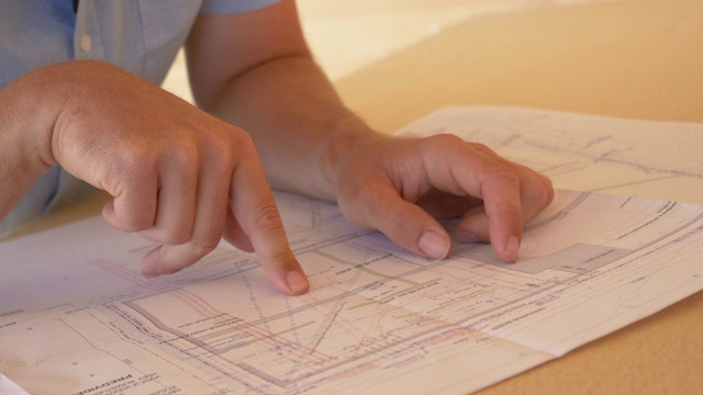 特写:一个面目全非的男人用手指在一幢房子的设计图上移动。视频下载