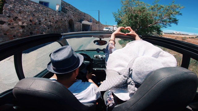 在希腊圣托里尼岛的乡村道路上，一个苗条的女孩和她的男朋友在一辆敞篷车上把手举向空中视频素材