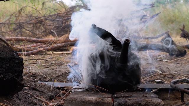 被煤烟熏黑的水壶在一个游客篝火上的篝火上沸腾视频素材