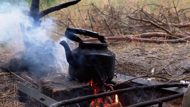 被煤烟熏黑的水壶在一个游客篝火上的篝火上沸腾视频素材